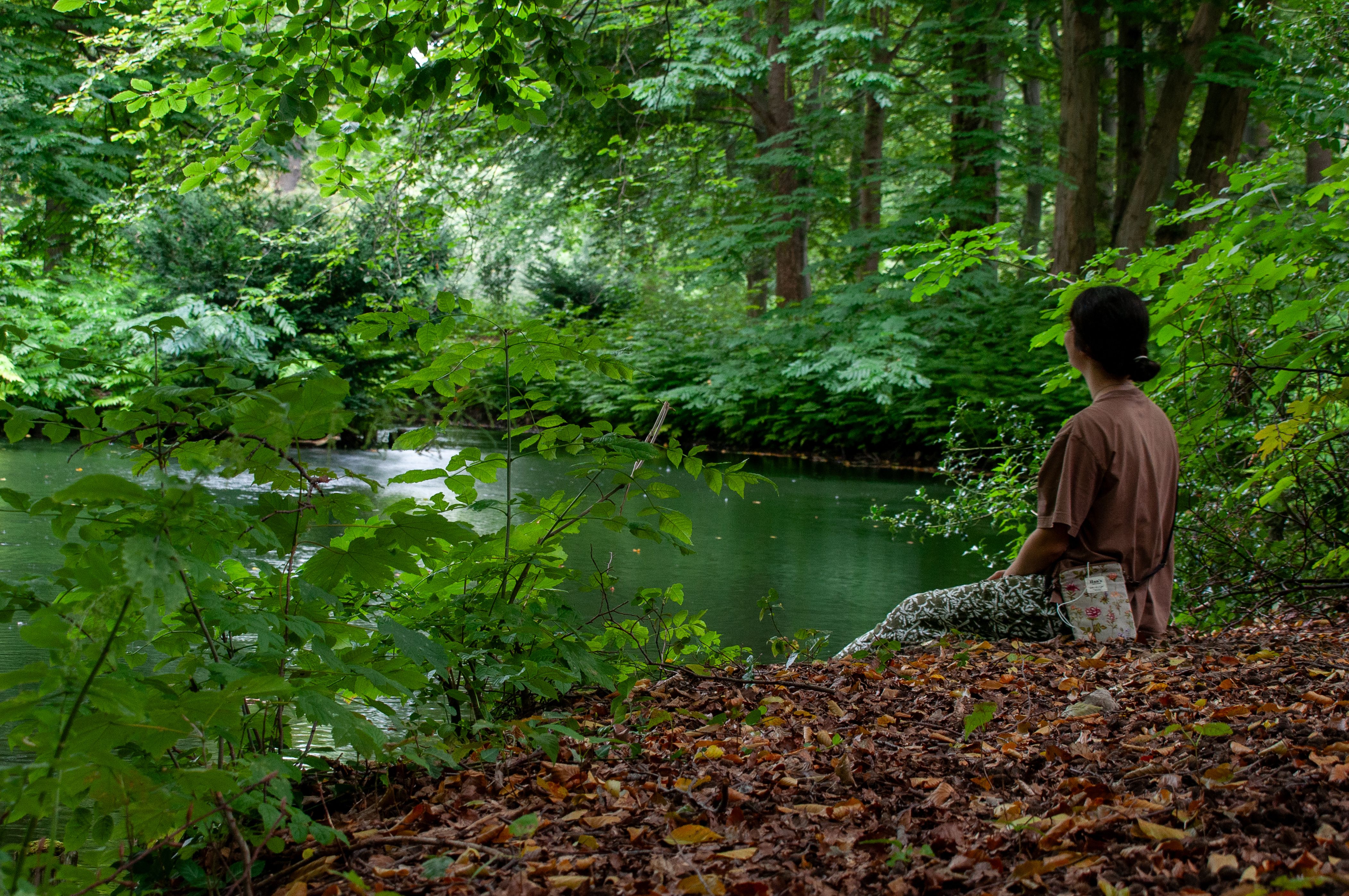 Person sitting by a calm wooded riverbank