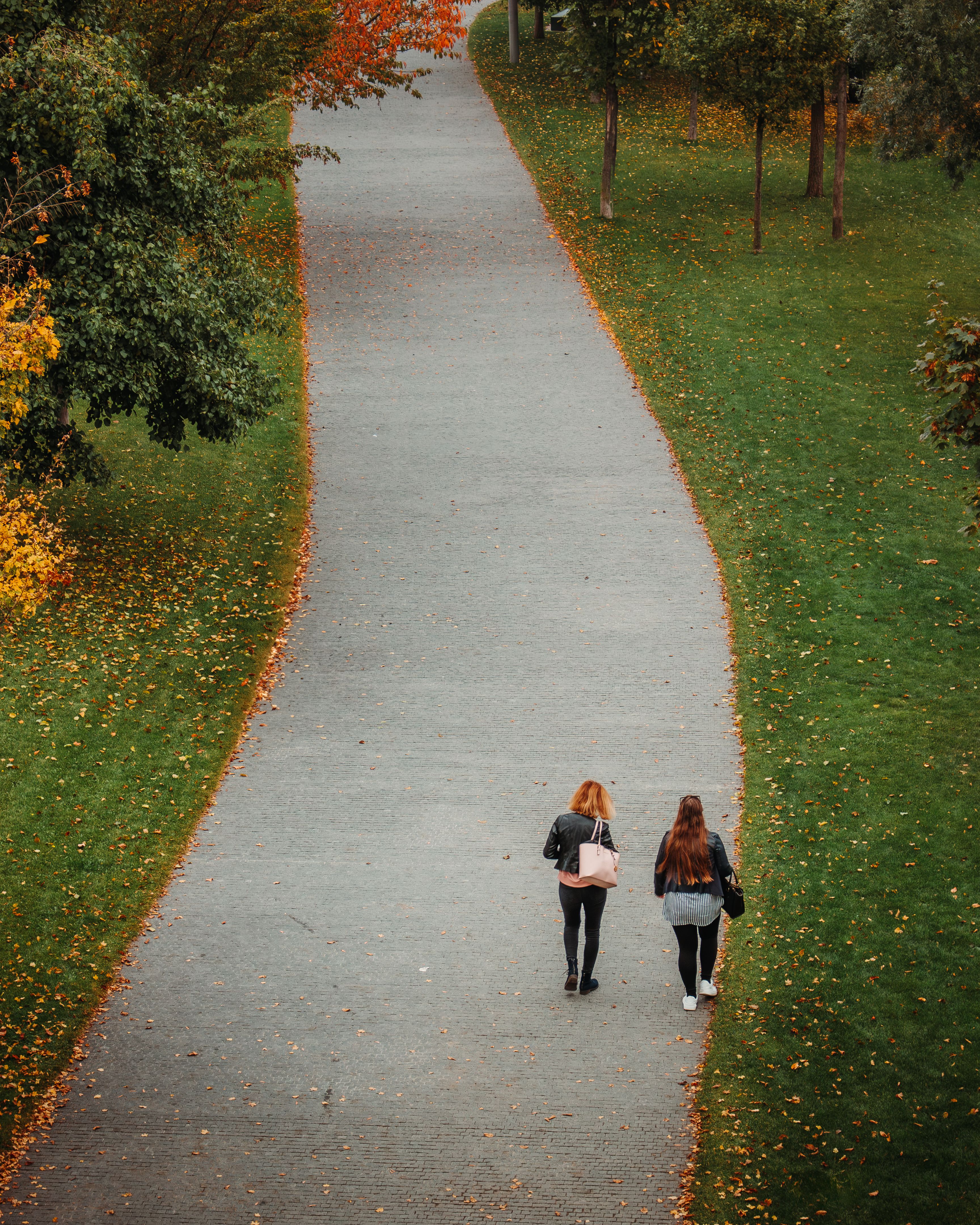 Two people walking side by side along a tree-lined path in an East Nashville park
